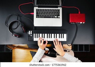 Top view of music composer playing MIDI keyboard and electric guitar to create music at home studio.