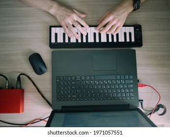 Top view of music producer or arranger using laptop, midi keyboard, and other audio equipmen to create music at home studio. Beat making, arranging audio content, composing song