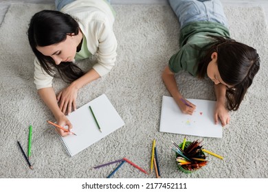 Top View Of Nanny And Girl Drawing On Papers While Lying On Carpet In Living Room