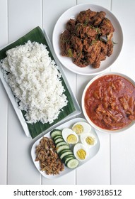 Top View Of Nasi Lemak With Chicken Rendang And Squid Sambal On White Wooden Background. Nasi Lemak Is A Malaysian Popular Favourite Food. Traditionally Nasi Lemak Is Wrapped With Banana Leaf. 