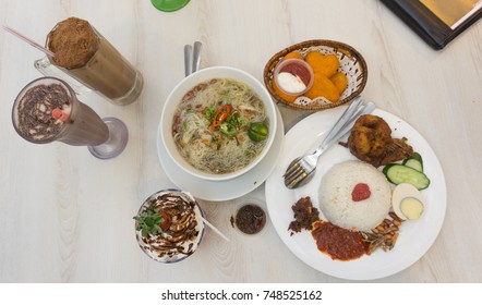 Top View Of Nasi Lemak, A Traditional Malay Curry Paste Rice Dish At The Restaurant With Other Side Dish And Drink