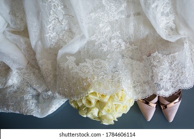 Top View Of The New Pair Of Stylish Blush Pink  High Heels Wedding Shoes And Wedding Bouquet Of Yellow Roses, White Lace Wedding Dress On The Background