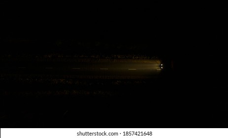  Top View Of The Night Road Along Which A Lonely Car Drives In The Middle Of The Forest And Shines With Headlights