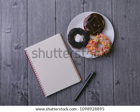 Top view of Notebook, ballpen, and doughnut on wooden background
