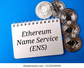 Top view notebook and eth coins with text Ethereum name service (ENS) on blue background.