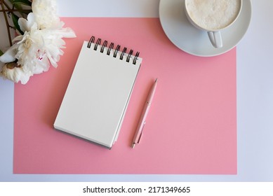 Top view of notebook with white empty page pink peonies and Feminine home office mock up with blank sheet of paper A4 portrait format, copy space for text. Flat lay. Pink peony and coffee
