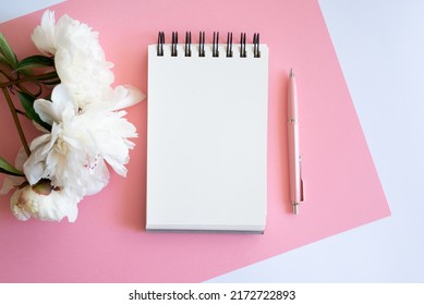 Top view of notebook with white empty page pink peonies and Feminine home office mock up with blank sheet of paper A4 portrait format, copy space for text. Flat lay. Pink peony and coffee