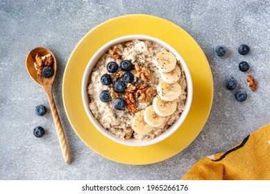 Top view of oatmeal in bowl on yellow plate with banana, nuts and berries.