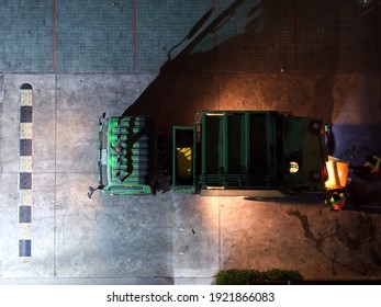 Top View Of, Green Garbage Truck At Night On Car Parking Lot With, Garbage Collector Working Near The Trunk.