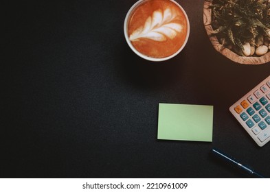 Top View Office Desk With Calculator, Coffee Mug, Pen And Cactus On Vintage Tone Black Background..Flat Lay Copy Space.