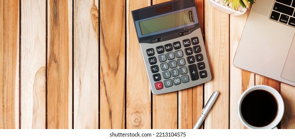 Top View Office Desk With Calculator, Pen, Computer Laptop, Plant Pot And Coffee Cup On Wood Table Background. Workspace Or Home Office With Copy Space For Text Concept