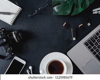 Top View Of Office Desk Concept With Coffee Cup, Digital Camera, Notebook, Plastic Plant And Smartphone On Black Table Background, Graphic Designer, Creative Designer Concept.