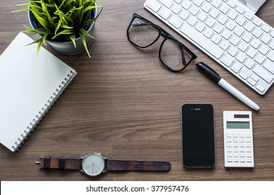 Top view of Office desk with keyboard,small green flower ,smart phone,watch,blank notebook and eyeglasses 