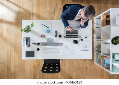 Top view at office. A grey hair businessman sitting at his desk and using a phone. Focus on the table