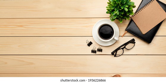 Top View Office Table Desk. Workspace With Blank, Office Supplies, Pencil, Green Leaf, And Coffee Cup On Wood Background.