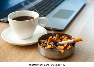 Top view office table desk. Workspace with  a cup of black coffee, laptop and dirty ashtray full cigarette butts. Unhealthy life style, Bad habits concept