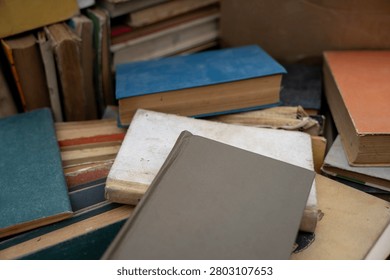 Top view of old antique and secondhand books piled haphazardly on asphalt ground, illustrating a flea market selection, garage sale clutter, or secondary paper waste recycling.