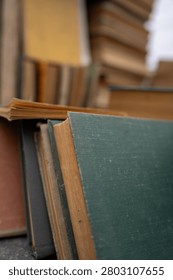 Top view of old antique and secondhand books piled haphazardly on asphalt ground, illustrating a flea market selection, garage sale clutter, or secondary paper waste recycling.