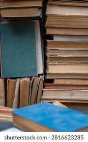 Top view of old antique and secondhand books piled haphazardly on asphalt ground, illustrating a flea market selection, garage sale clutter, or secondary paper waste recycling.