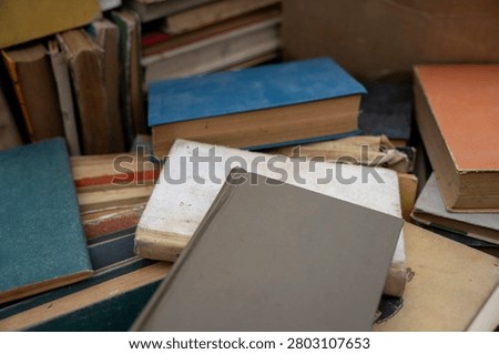 Top view of old antique and secondhand books piled haphazardly on asphalt ground, illustrating a flea market selection, garage sale clutter, or secondary paper waste recycling.