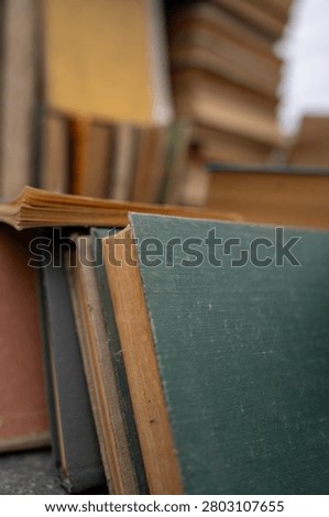 Top view of old antique and secondhand books piled haphazardly on asphalt ground, illustrating a flea market selection, garage sale clutter, or secondary paper waste recycling.