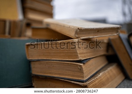 Top view of old antique and secondhand books piled haphazardly on asphalt ground, illustrating a flea market selection, garage sale clutter, or secondary paper waste recycling.