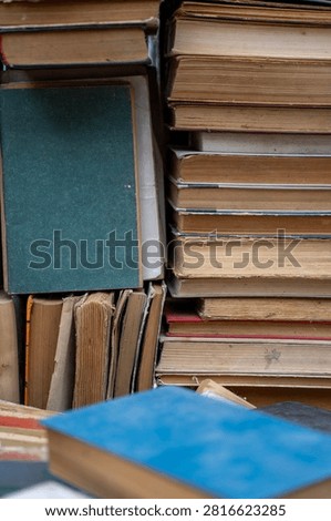 Top view of old antique and secondhand books piled haphazardly on asphalt ground, illustrating a flea market selection, garage sale clutter, or secondary paper waste recycling.