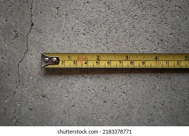 Top View Of Old Rusty Chrome Metal Yellow Measuring Tape On Concrete Garage Floor. 