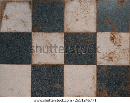 Top view of an old, weathered ceramic tile floor with a classic black and white checkerboard pattern. The surface shows signs of dirt, rust stains, and wear and giving a vintage.
