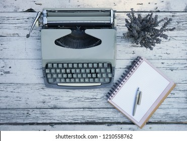 Top view of old wooden table with a typewriter, spiral notepad, old fashioned pen and a bouquet of lavender flovers. Vintage, romantic desk composition.