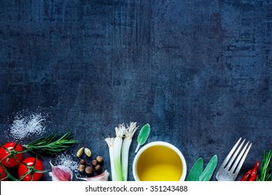 Top view of olive oil and fresh cooking ingredients (young green onions, peppercorns, tomatoes, garlic, rosemary) on dark vintage background. Top view. Cooking, Healthy Eating or Vegetarian concept.