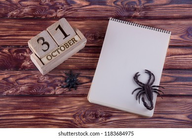 Top View On Blank Paper Notepad Laying On Wooden Table Near Spider, Scorpio And Cube Calendar With Halloween Date. Space For Text