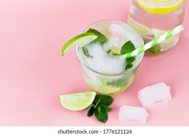 Top View On A Carafe With Refreshing Water With Lemon Or Lime And Ice And In The Foreground A Glass With A Cocktail On A Pink Background. Summer Cold Drinks