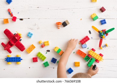 Top view on child playing and building with colorful plastic bricks at white wooden table. Early learning and development.