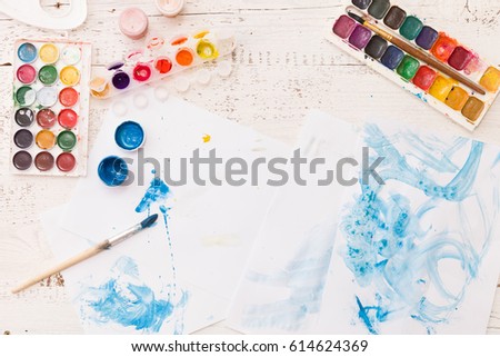 Top view on child's drawings and colorful paints and brushes. Creative ideas, creativity and early learning. Education concept.