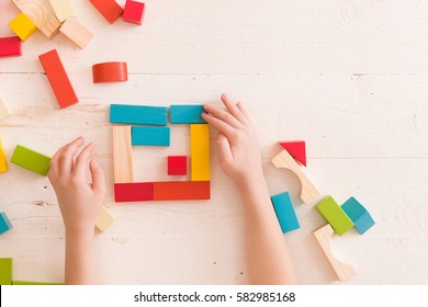 Top view on child's hands playing with colorful wooden bricks on the white table background.Kid building with geometric shapes. Learning and education concept.