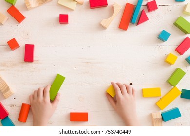 Top view on child's hands playing with colorful wooden bricks on white table background. Boy building with wooden constructor. Education concept