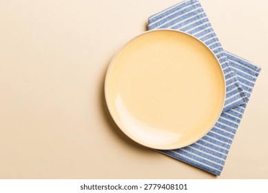 Top view on colored background empty round yellow plate on tablecloth for food. Empty dish on napkin with space for your design.