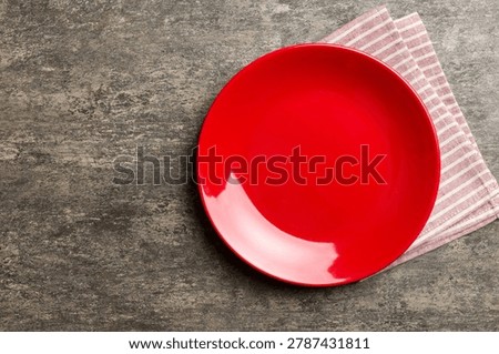 Top view on colored background empty round red plate on tablecloth for food. Empty dish on napkin with space for your design.