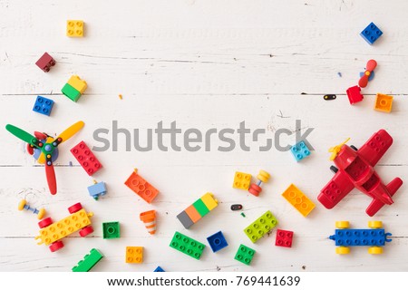 Top view on colorful plastic toy bricks and details on white wooden background