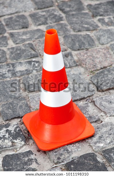 The top view on cone zone,\
orange road cone with white stripes on the road from paving\
stones.
