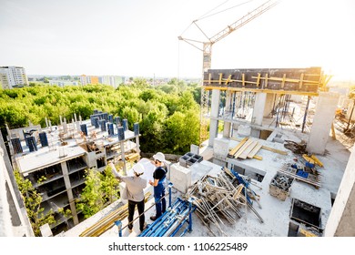 Top View On The Construction Site Of Residential Buildings During The Construction Process With Two Workers Standing With Drawings