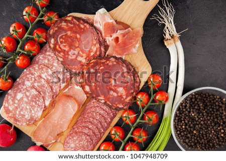 Top view on different types of sliced ham, proscuitto and salami next to cherry tomatoes, green onion and radish