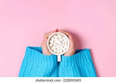 Top view on Girls hands in blue cozy oversized sweater holding large cup of cocoa or hot chocolate isolated on pink background.