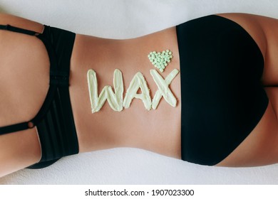 Top view on inscription "wax" laid out with hot wax for depilation. Heart which composed of granules of depilatory wax. Hair removal procedure on female back. The concept of epilation, waxing