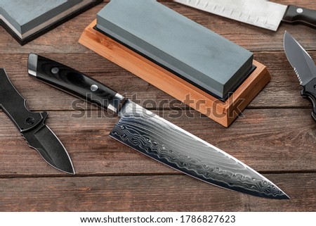 Top view on Japanese chef's and Santoku knives, pocket knives and whetstones on wooden background.
