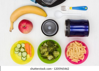 Top View On Lunch Box, Thermos And Healthy Food Options For School On Old White Wooden Table. Snacks For The Day. Hot Lunch, Take Away. Cucumbers, Carrots, Broccoli, Apple, Banana And Pasta.