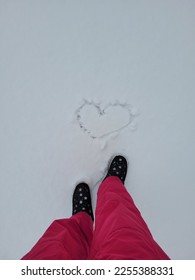Top view on the men legs in viva magenta ski pants and  winter shoes in snow. The person stands near the heart painted on the snow. Valentines day concept. - Shutterstock ID 2255388331