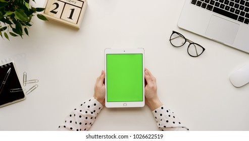 Top View On The Office Desk And White Tablet Computer With Green Screen And Female Hands Taping On It. Vertical. Office Stuff Beside. Chroma Key.