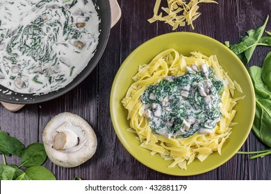 Top View on Pasta with Spinach, Cream and Champignon Mushrooms on Green Plate on Dark Wooden Table